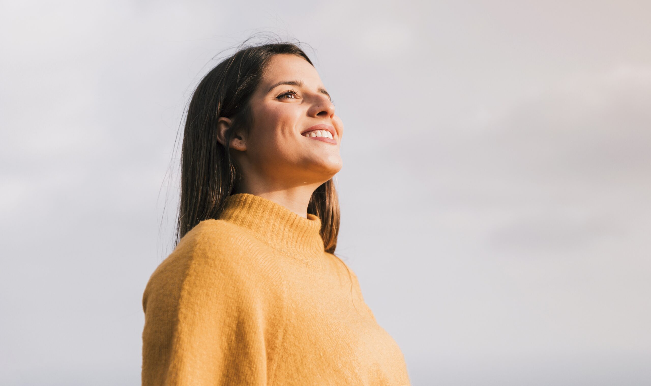 smiling-young-woman-standing-against-sky-looking-away